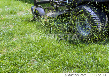 Lawn mower cuts grass in residential yard on summer season Lawn mower cuts grass in residential yard on summer season 135572161
