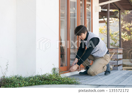一名身穿工作服的男子正在修理窗戶。 一名身穿工作服的男子正在修理窗戶。 135572172