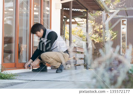 一名身穿工作服的男子正在修理窗戶。 一名身穿工作服的男子正在修理窗戶。 135572177