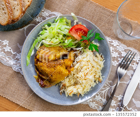 Tender meat of roasted chicken is garnished with boiled rice, vegetable salad. 135572352