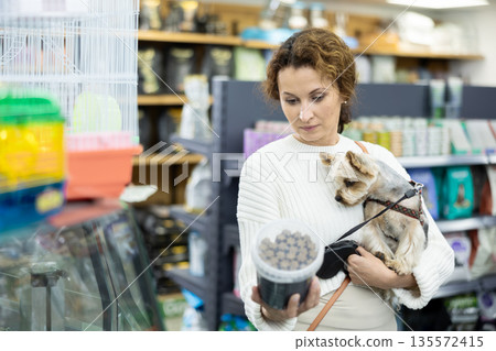 Female owner of Yorkshire terrier choosing dry dog food in pet store 135572415