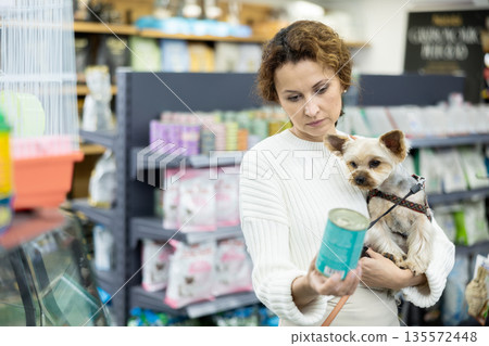 Female owner of Yorkshire terrier choosing canned dog food in pet store Female owner of Yorkshire terrier choosing canned dog food in pet store 135572448