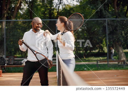 Sumer season. Young black guy with racket and girl having conversation at playground. Tennis, hobbies. Sumer season. Young black guy with racket and girl having conversation at playground. Tennis, hobbies. 135572449