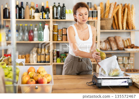 Adult woman seller weighs pears in bag 135572467