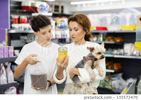 Mother with dog Yorkshire Terrier in arms and son carefully examine label on dry dog food Mother with dog Yorkshire Terrier in arms and son carefully examine label on dry dog food 135572470