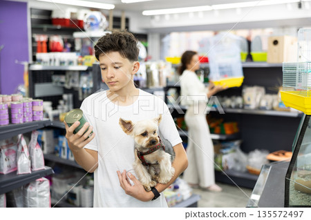 Teenager with Yorkshire terrier choosing canned dog food in pet store Teenager with Yorkshire terrier choosing canned dog food in pet store 135572497