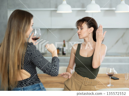 Two joyful middle-aged women dancing together at the kitchen-table with wineglasses 135572552