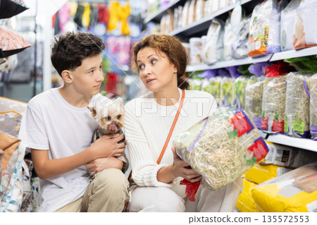 Woman with teenage son and Yorkshire terrier choosing straw bedding in pets store Woman with teenage son and Yorkshire terrier choosing straw bedding in pets store 135572553
