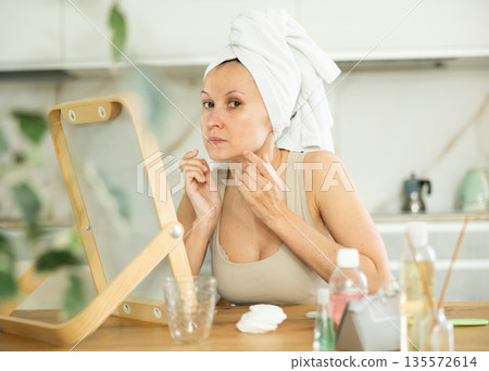 Middle-aged woman examining her facial skin looking in the mirror put on the table 135572614