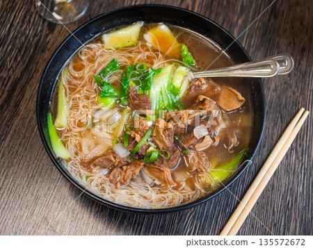 Deep clay bowl is filled with hot noodle soup and veal fillet. Deep clay bowl is filled with hot noodle soup and veal fillet. 135572672