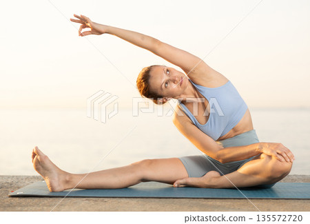 Near sea during sunset, girl performs variations of Janu Shirshasana Near sea during sunset, girl performs variations of Janu Shirshasana 135572720