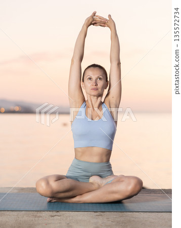Near sea during sunset, girl performs variations of padmasana Near sea during sunset, girl performs variations of padmasana 135572734