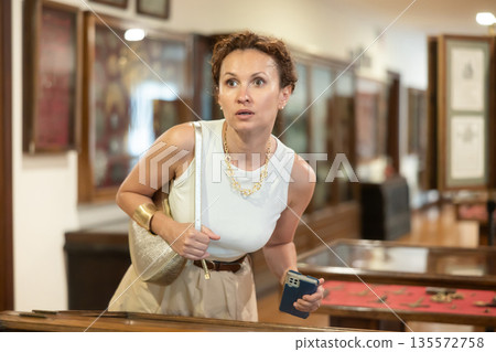 Woman curiously observing antique artifacts in historical museum 135572758