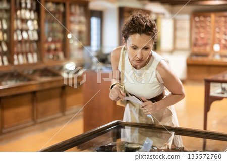 Woman examining antique artifacts within glass vitrine in museum 135572760