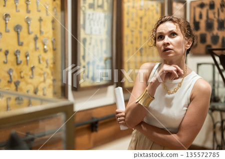 Woman with sheet piece of paper in her hands walks around museum hall Woman with sheet piece of paper in her hands walks around museum hall 135572785