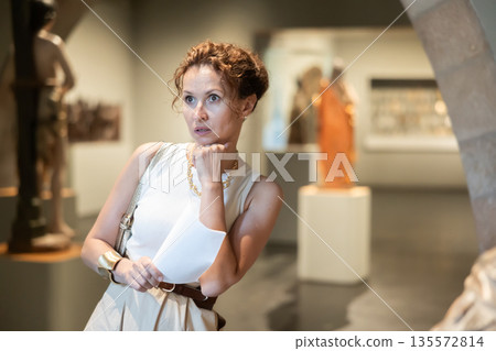 Woman with sheet piece of paper in her hands walks around museum hall Woman with sheet piece of paper in her hands walks around museum hall 135572814
