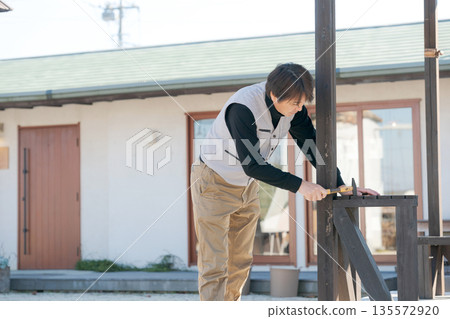 一名身穿工作服的男子正在修繕房屋 一名身穿工作服的男子正在修繕房屋 135572920