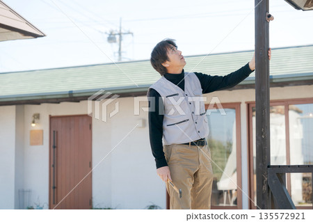 一名身穿工作服的男子正在修繕房屋 一名身穿工作服的男子正在修繕房屋 135572921