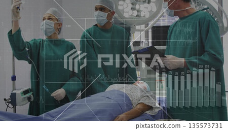 Adjusting IV drip anesthesiologist working with team around patient in OR, with ECG monitor 135573731