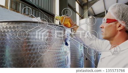 Inspecting technician in lab gear sampling amber liquid with beaker by tank in brewery, copy space 135573766