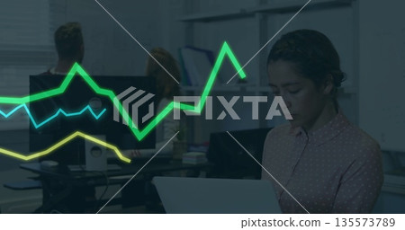 Analyzing woman in patterned blouse using laptop in office with colored graph lines, copy space Analyzing woman in patterned blouse using laptop in office with colored graph lines, copy space 135573789