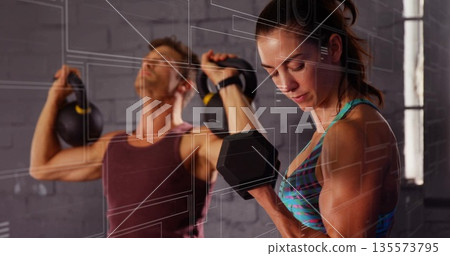 Performing single-arm dumbbell curl woman and lifting kettlebells man training inside brick gym Performing single-arm dumbbell curl woman and lifting kettlebells man training inside brick gym 135573795