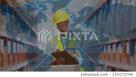 Inspecting boxes man wearing hard hat and vest using clipboard in warehouse aisle, with map overlay 135573799