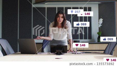 Presenting woman wearing blouse leaning on conference table with laptop speakerphone and smartphone 135573892