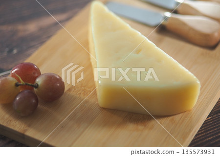 Cheese and grapes on a wooden cutting board Cheese and grapes on a wooden cutting board 135573931