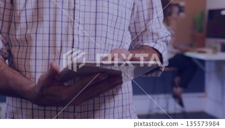 Tapping office worker wearing checkered shirt holding tablet computer in open-plan office Tapping office worker wearing checkered shirt holding tablet computer in open-plan office 135573984