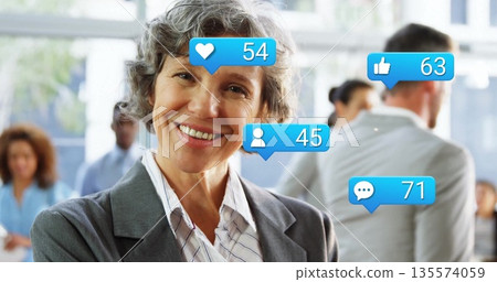 Smiling senior businesswoman wearing gray blazer, striped shirt in office with social media icons 135574059
