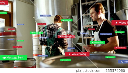 Holding tablet, brewery worker wearing apron inspecting tanks with overlays in brewery, copy space 135574060