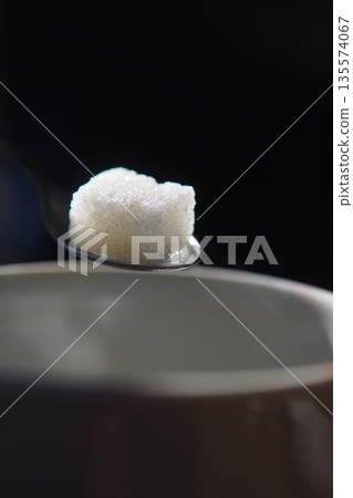 Spoon with sugar near a brown cup on a dark surface Spoon with sugar near a brown cup on a dark surface 135574067