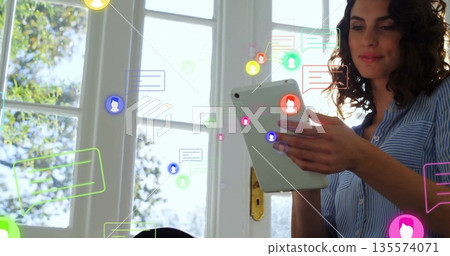 Holding tablet woman with striped shirt sitting home by white window with chat bubbles, copy space Holding tablet woman with striped shirt sitting home by white window with chat bubbles, copy space 135574071