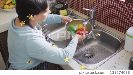 Rinsing Senior Indian woman holding metal colander at kitchen sink, cleaning colorful bell peppers Rinsing Senior Indian woman holding metal colander at kitchen sink, cleaning colorful bell peppers 135574088