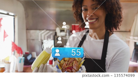 Serving server in apron offering hot dog with fries, mustard bottle in truck kitchen, copy space Serving server in apron offering hot dog with fries, mustard bottle in truck kitchen, copy space 135574099