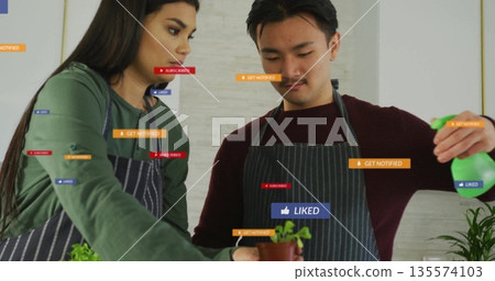 Spraying man and colleague watering herb plants in striped aprons in kitchen with digital icons Spraying man and colleague watering herb plants in striped aprons in kitchen with digital icons 135574103