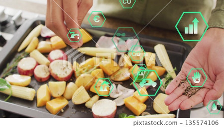Sprinkling green-shirted woman's hands seasoning vegetables on tray in kitchen, with digital icons 135574106