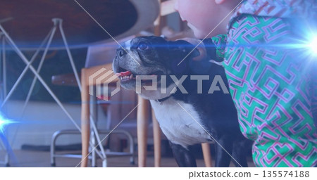 Boy wearing green geometric top kneeling on floor in dining area, petting black-and-white dog Boy wearing green geometric top kneeling on floor in dining area, petting black-and-white dog 135574188