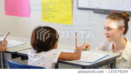 Guiding female student through math problems at classroom desk, with pencils and pink sticky notes Guiding female student through math problems at classroom desk, with pencils and pink sticky notes 135574204
