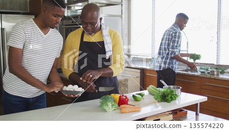 Slicing father in yellow shirt and apron, son cutting mushrooms on kitchen island with vegetables 135574220