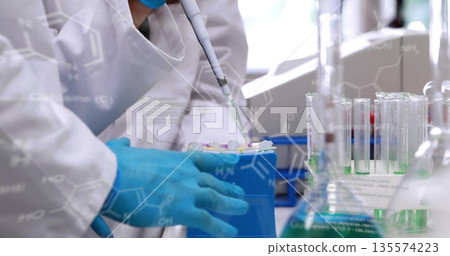 Scientist in lab coat transferring liquid using pipette at bench, with tubes, formulas, copy space 135574223