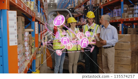 Coordinating team in vests and helmets viewing AR hologram in warehouse aisle, with forklift 135574257