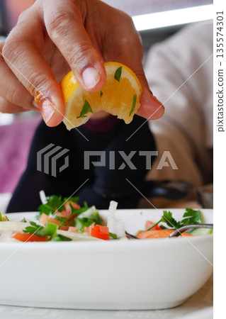 Fresh lemon being squeezed over a vibrant salad at a cafe Fresh lemon being squeezed over a vibrant salad at a cafe 135574301