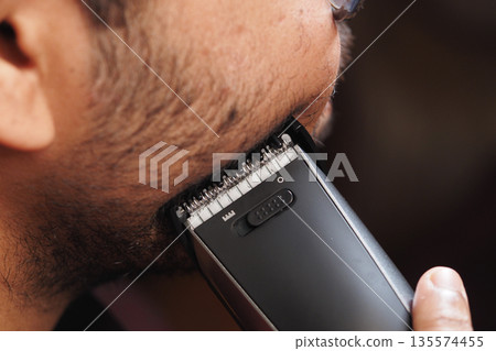 Close-up of a man trimming his beard with an electric clipper Close-up of a man trimming his beard with an electric clipper 135574455