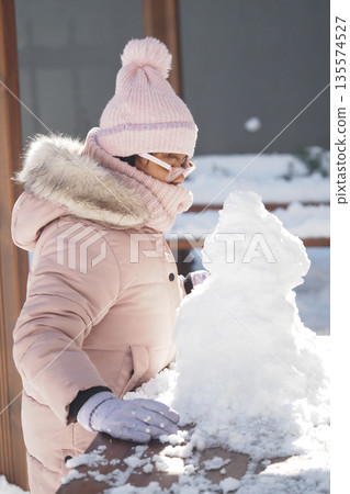 Child builds snowman in winter sunlight with warm clothes Child builds snowman in winter sunlight with warm clothes 135574527