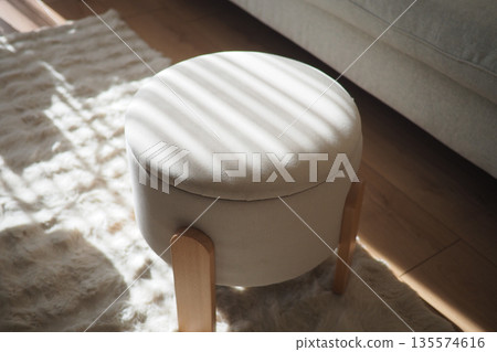 Soft ottoman sits in sunlight indoors on a rug Soft ottoman sits in sunlight indoors on a rug 135574616