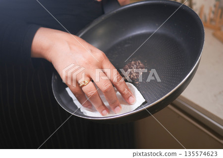 Cleaning a frying pan with paper towel in a kitchen 135574623