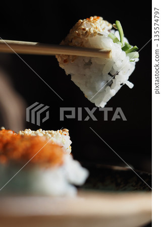 Sushi held with chopsticks over a wooden plate Sushi held with chopsticks over a wooden plate 135574797