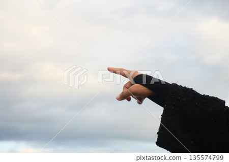Hand points towards the sky in a cloudy setting 135574799